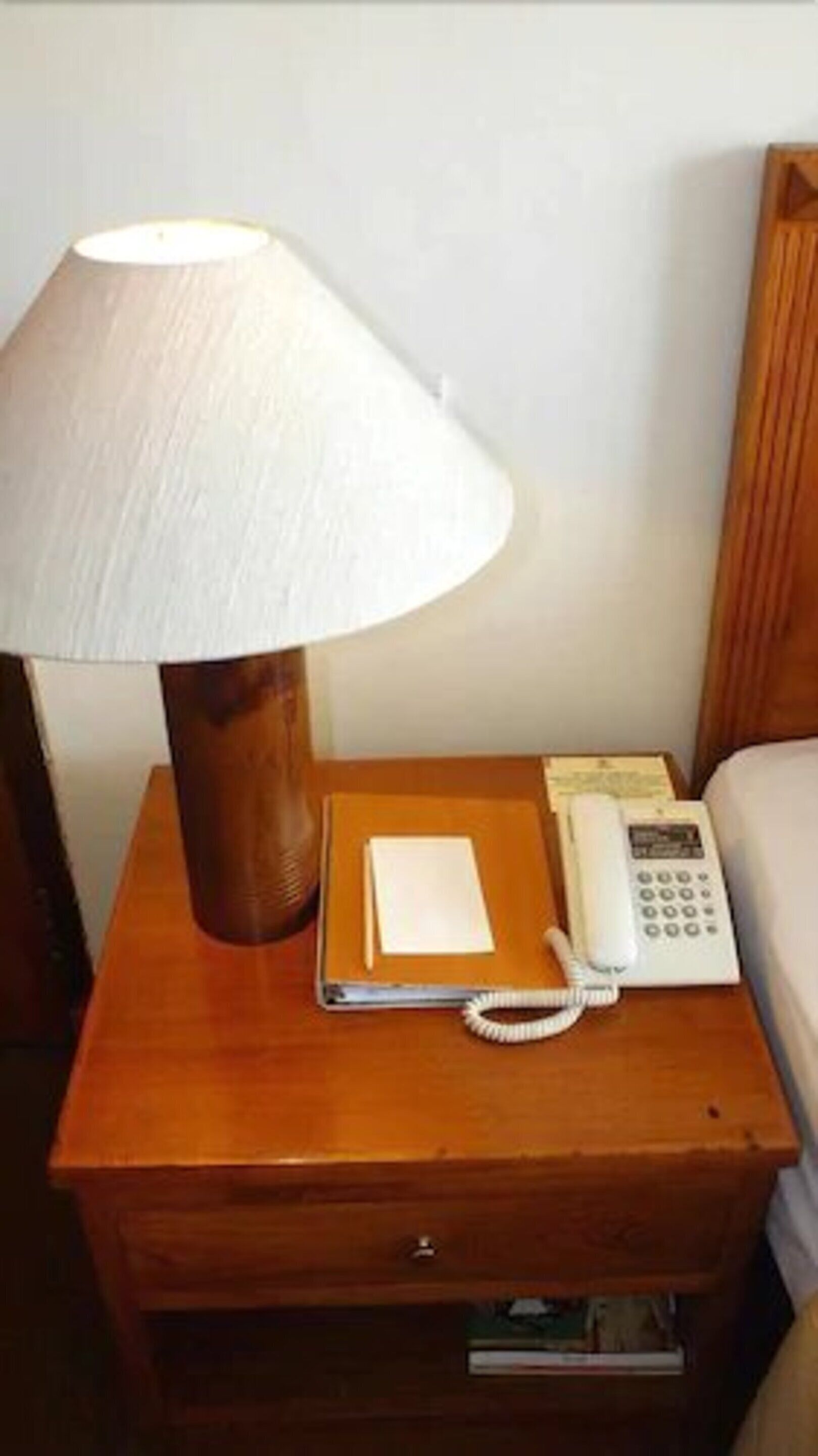 A wooden nightstand with a lamp, a telephone, a notepad, and a pen.