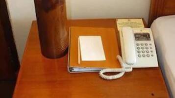A wooden nightstand with a lamp, a telephone, a notepad, and a pen.