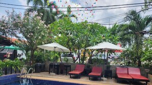 A swimming pool with red lounge chairs and umbrellas, surrounded by greenery and a stone wall. - Jasmine Lodge (Siem Reap)