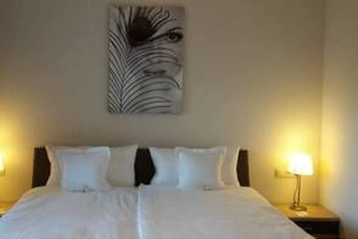 Quarto de hotel com uma cama grande, duas mesas de cabeceira com abajures e uma obra de arte na parede acima da cama.