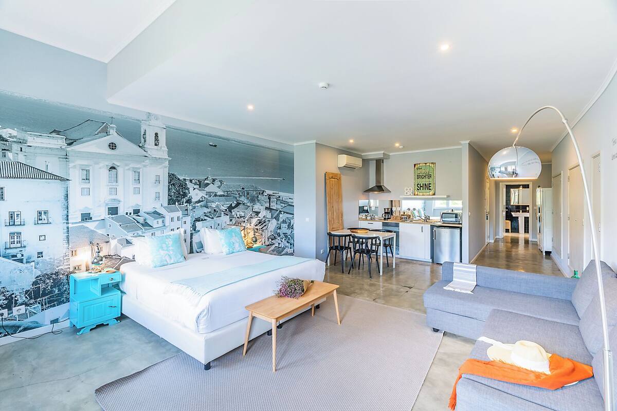 A modern apartment with a large bed, a dining area, and a kitchen.