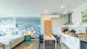 A modern bedroom with a large bed, a small bedside table, and a view of a coastal town. - Emporium Lisbon Suites (Lisbon)