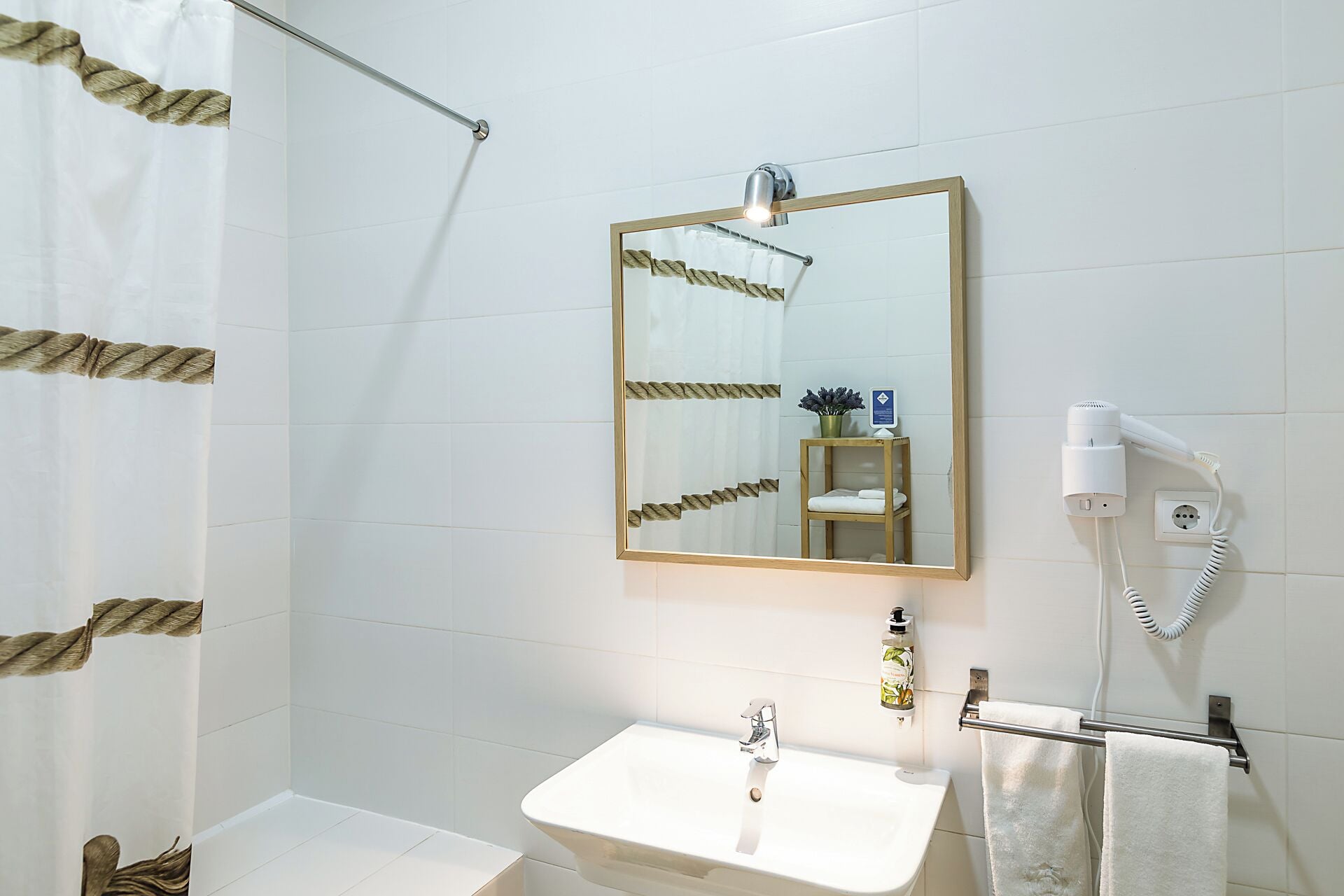 Uma casa de banho com uma pia branca, um espelho, um porta-toalhas, um secador de cabelo e uma cortina de chuveiro.