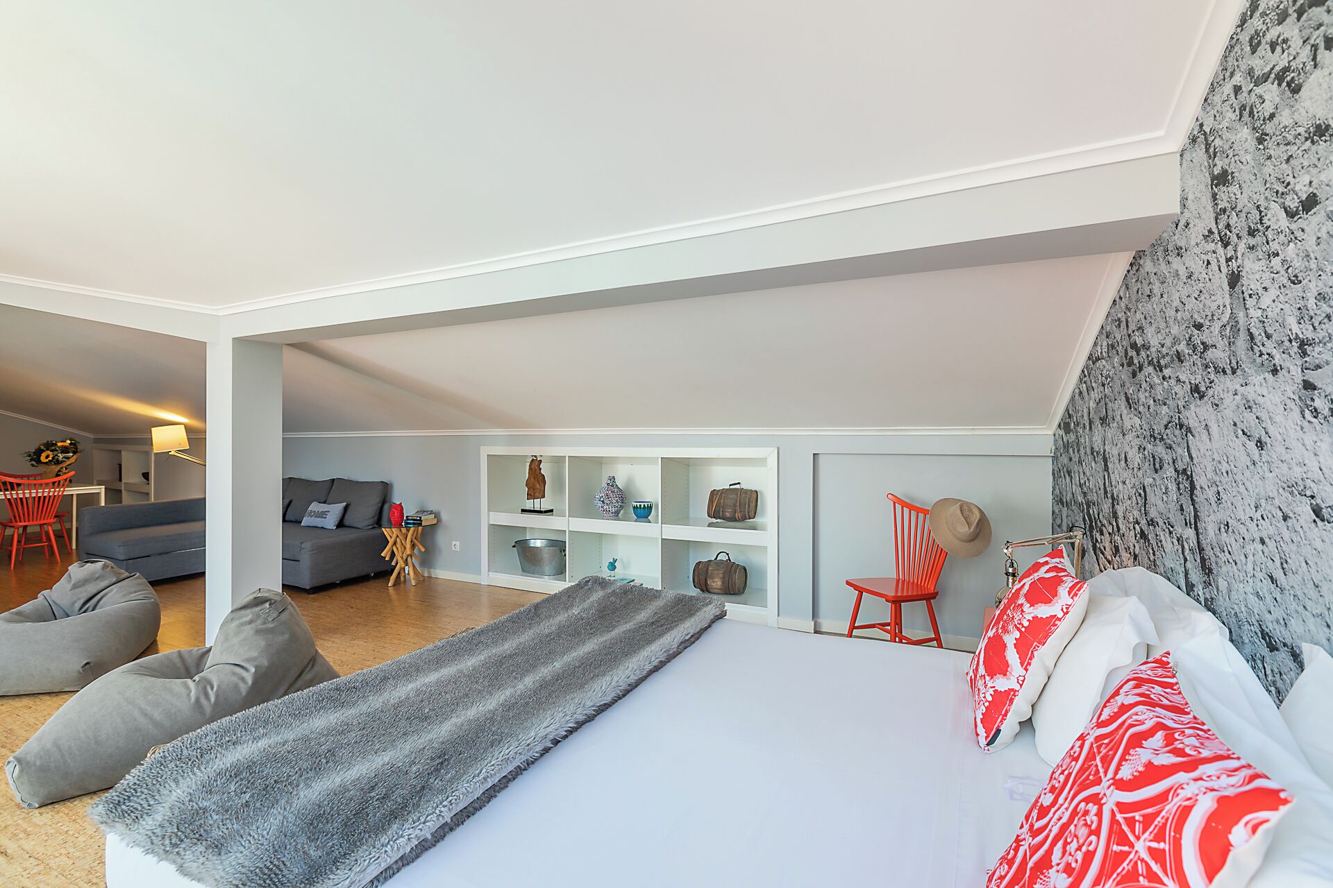 A modern bedroom with a large bed, grey and red pillows, a grey throw blanket, and a white headboard.