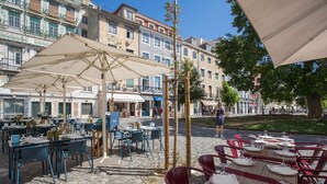 An outdoor café with tables and chairs, surrounded by buildings with balconies and storefronts. - Emporium Lisbon Suites (Lisbon)