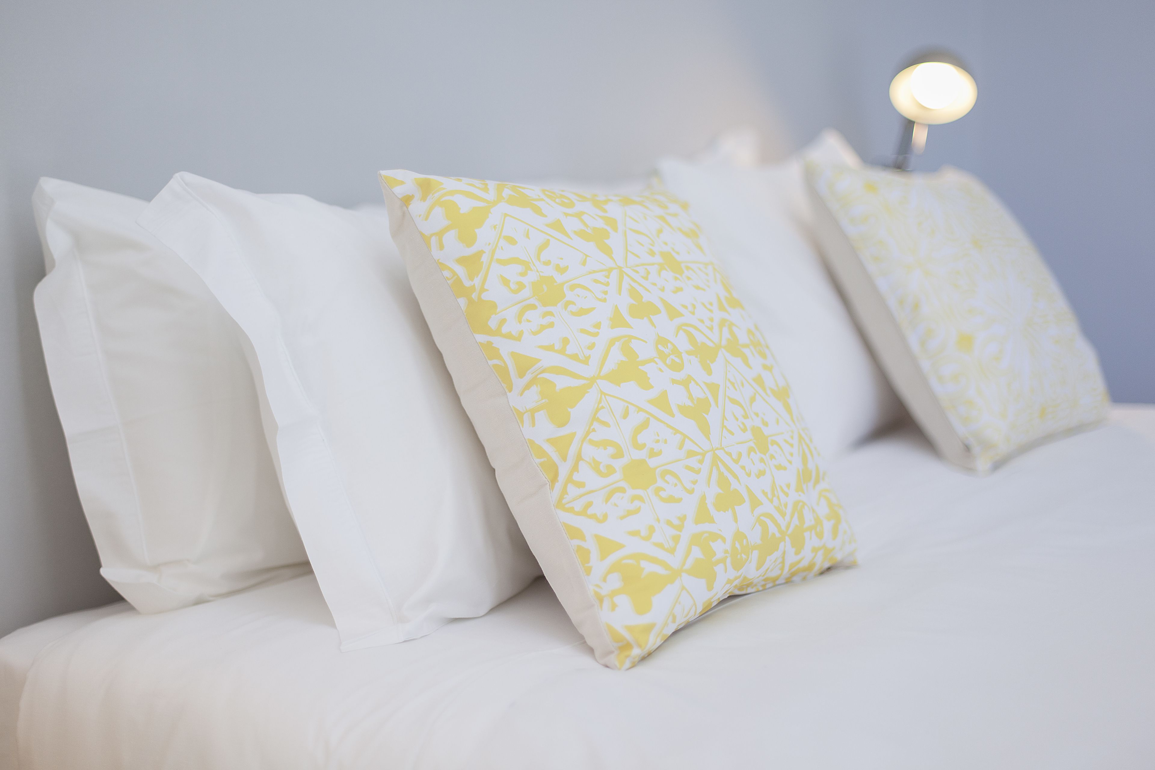 A bed with white and yellow patterned pillows and a bedside lamp.