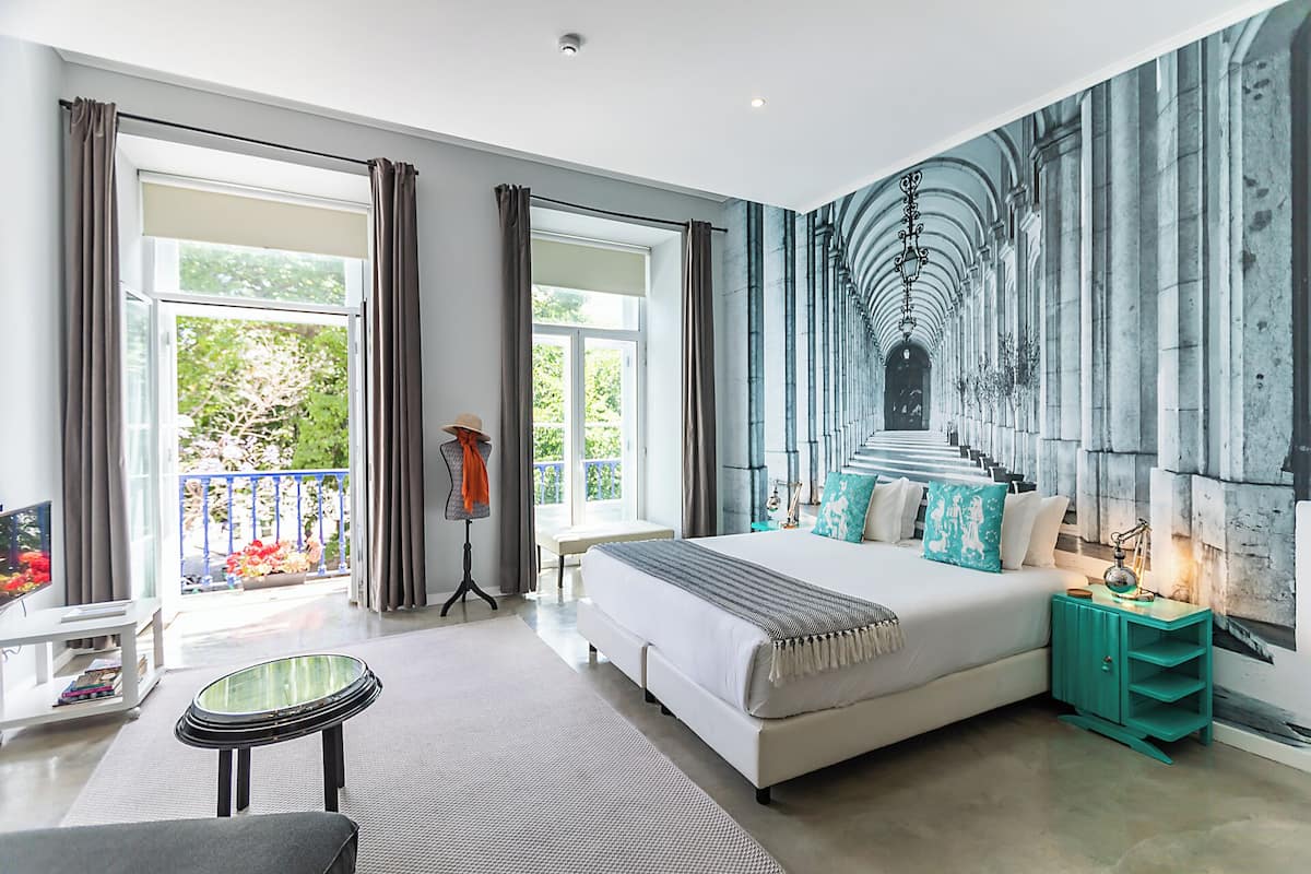 A modern bedroom with a large bed, a view of greenery outside, and a mural on the wall.