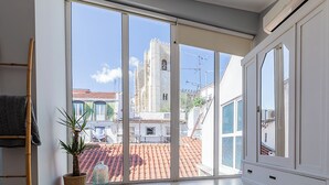 A room with a large sliding glass door leading to a terrace with a tiled roof, a view of a historic building, and a white wardrobe. - Emporium Lisbon Suites (Lisbon)