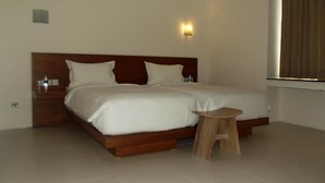A double bed with a wooden headboard, a small wooden stool, and a nightstand with a lamp. - L Bajo Hotel (Labuan Bajo)