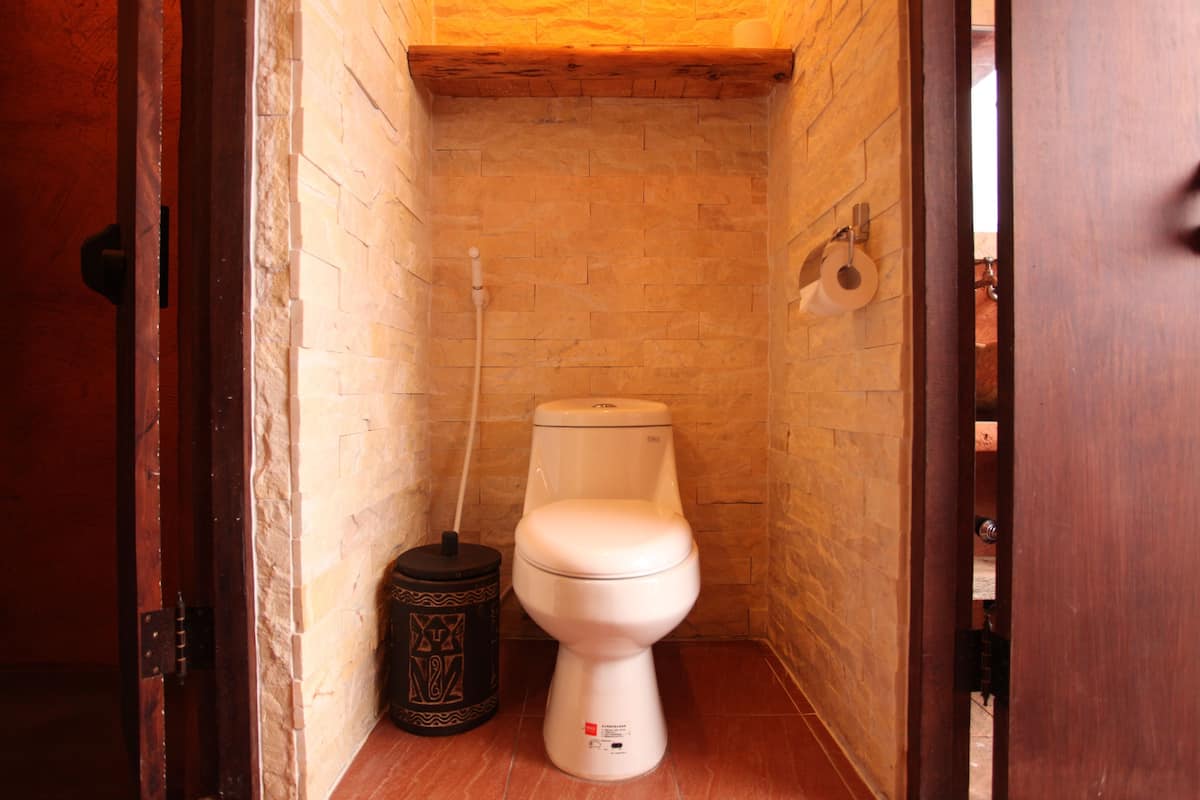 Ein kleines, schmales Badezimmer mit einer weißen Toilette, einem schwarzen Mülleimer und einem hölzernen Türrahmen.