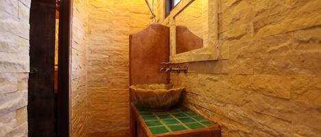 Un baño con pared de piedra, un lavabo de madera y encimera verde de azulejos, y una ducha con cabezal de ducha manual.