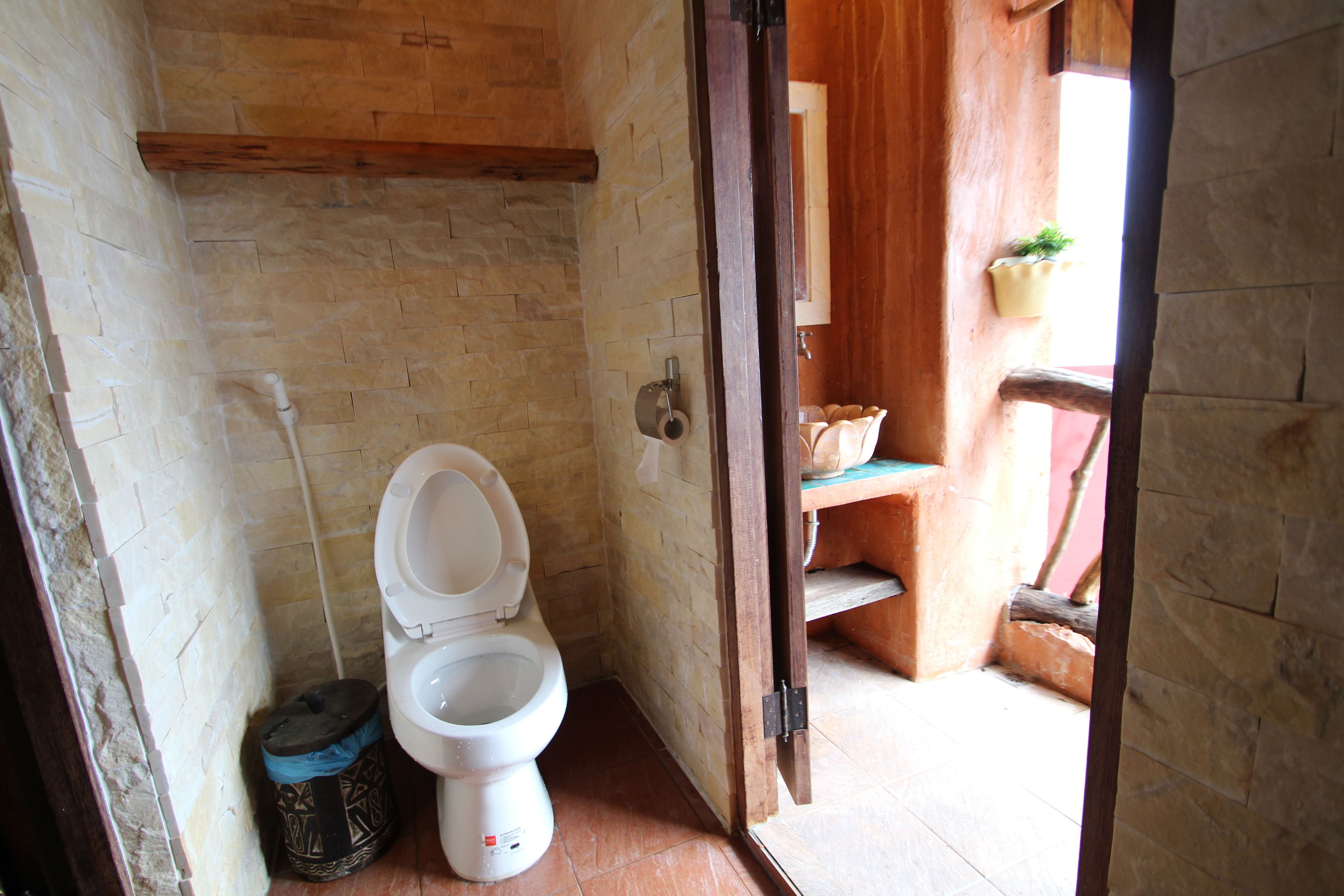 A small bathroom with a toilet, a wooden shelf, and a wooden door leading to another room.