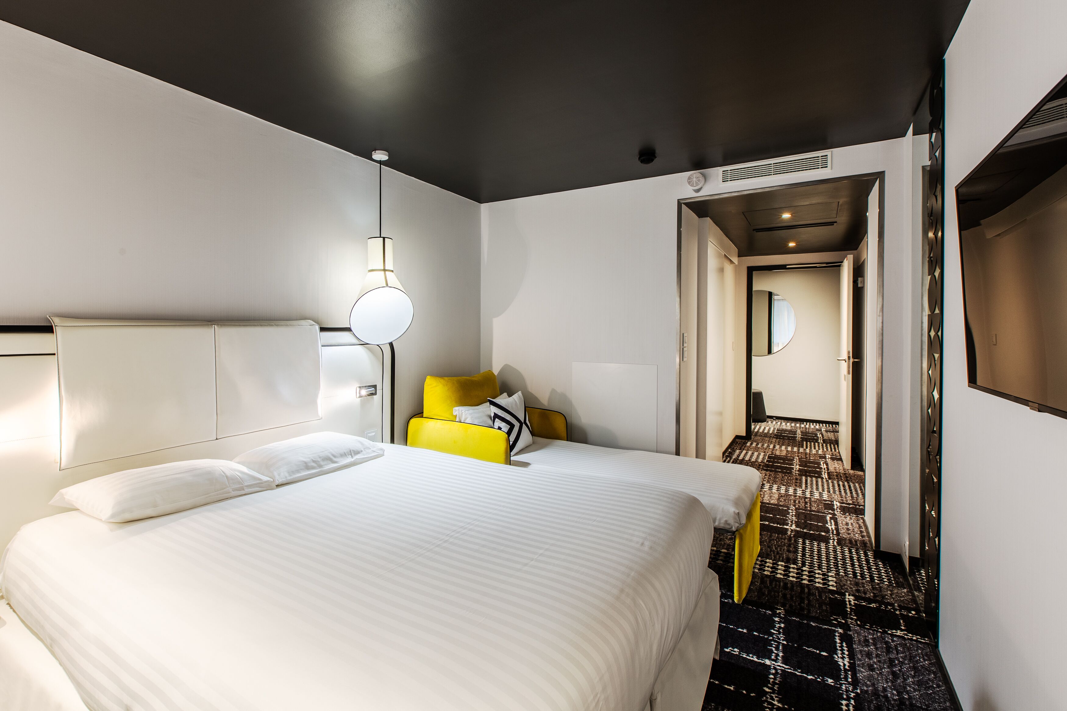 A hotel room with a large bed, a bedside table, a chair, and a mirror.