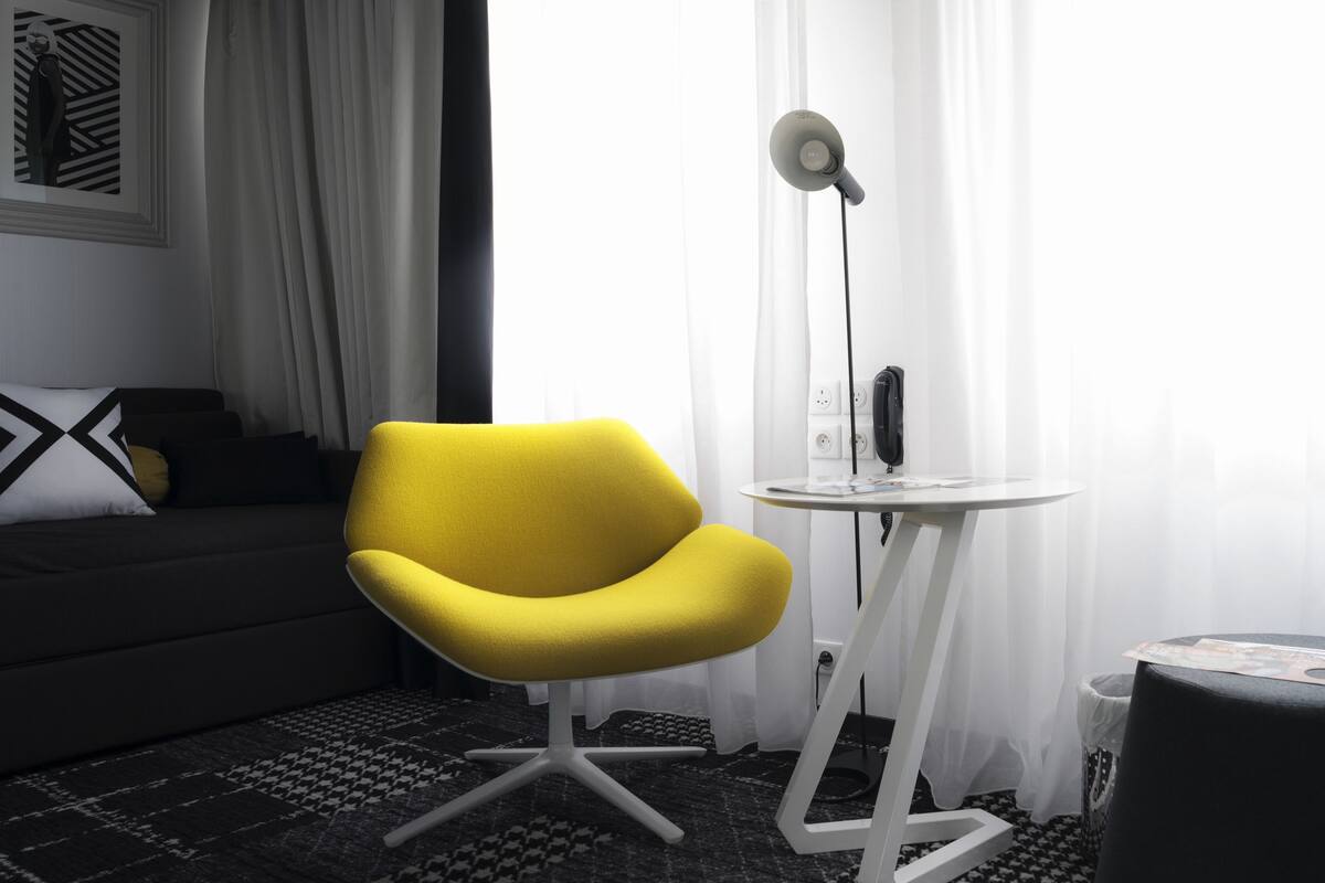 A modern room with a yellow armchair, a small white table, a floor lamp, and a grey sofa.