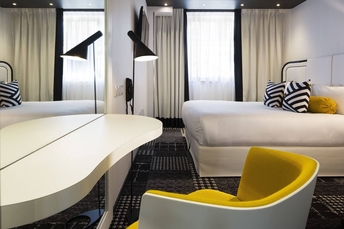 A hotel room with a bed, a desk, a chair, and a large window with curtains.