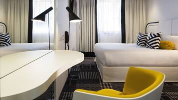 Quarto de hotel com uma cama, escrivaninha, cadeira e uma janela grande com cortinas.