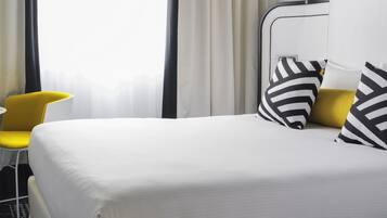 A modern hotel room with a large bed, a yellow chair, and a large window with curtains.