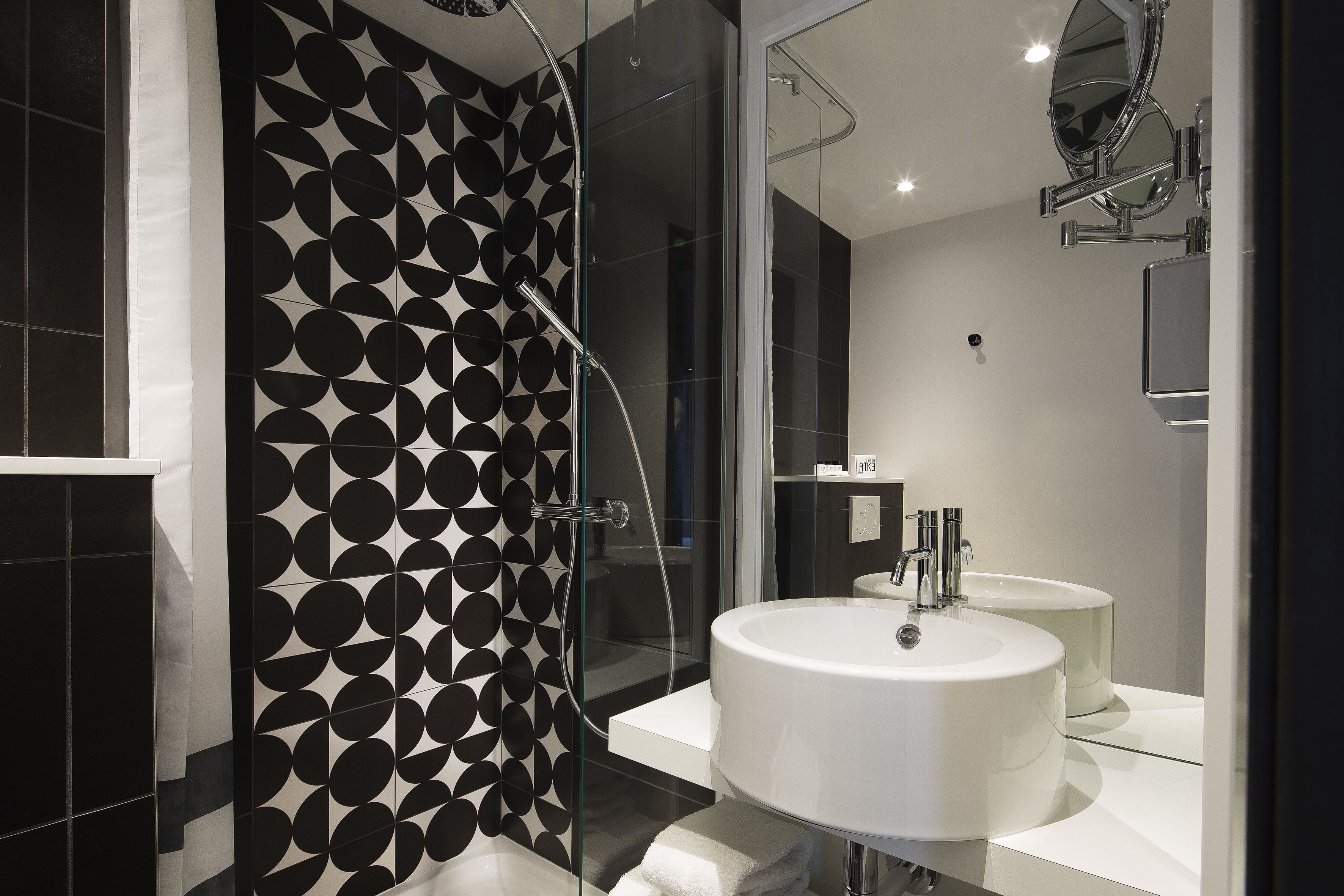 A modern bathroom with a glass shower enclosure, a white sink, and a black and white patterned wall.