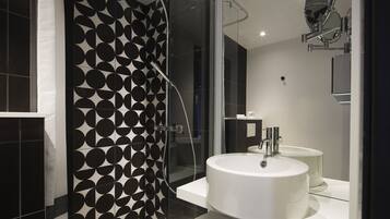 A modern bathroom with a glass shower enclosure, a white sink, and a black and white patterned wall.