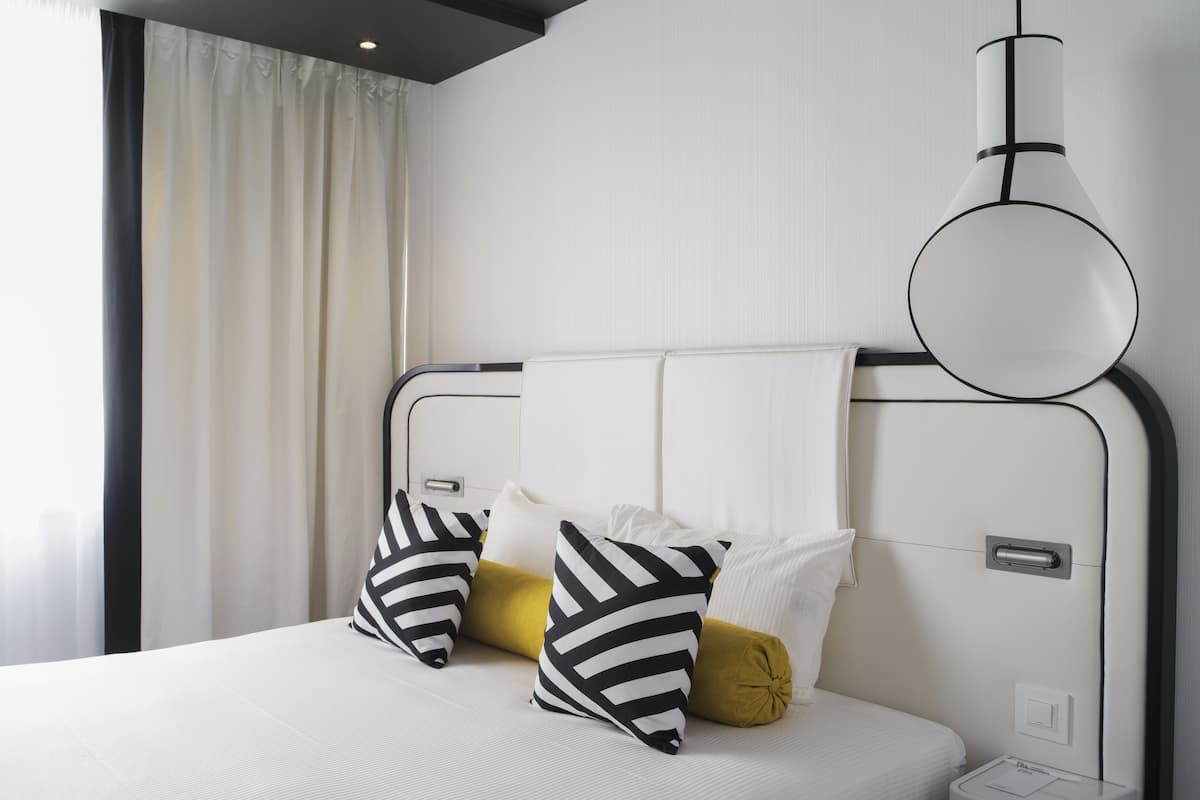 A modern hotel room with a neatly made bed, a bedside table, and a wall-mounted lamp.