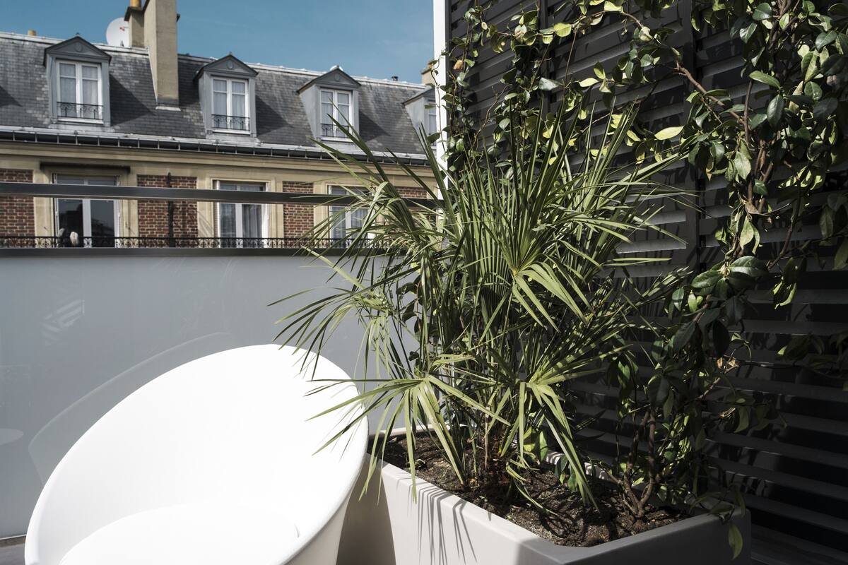 A balcony with a white chair, a potted plant, and a building in the background.