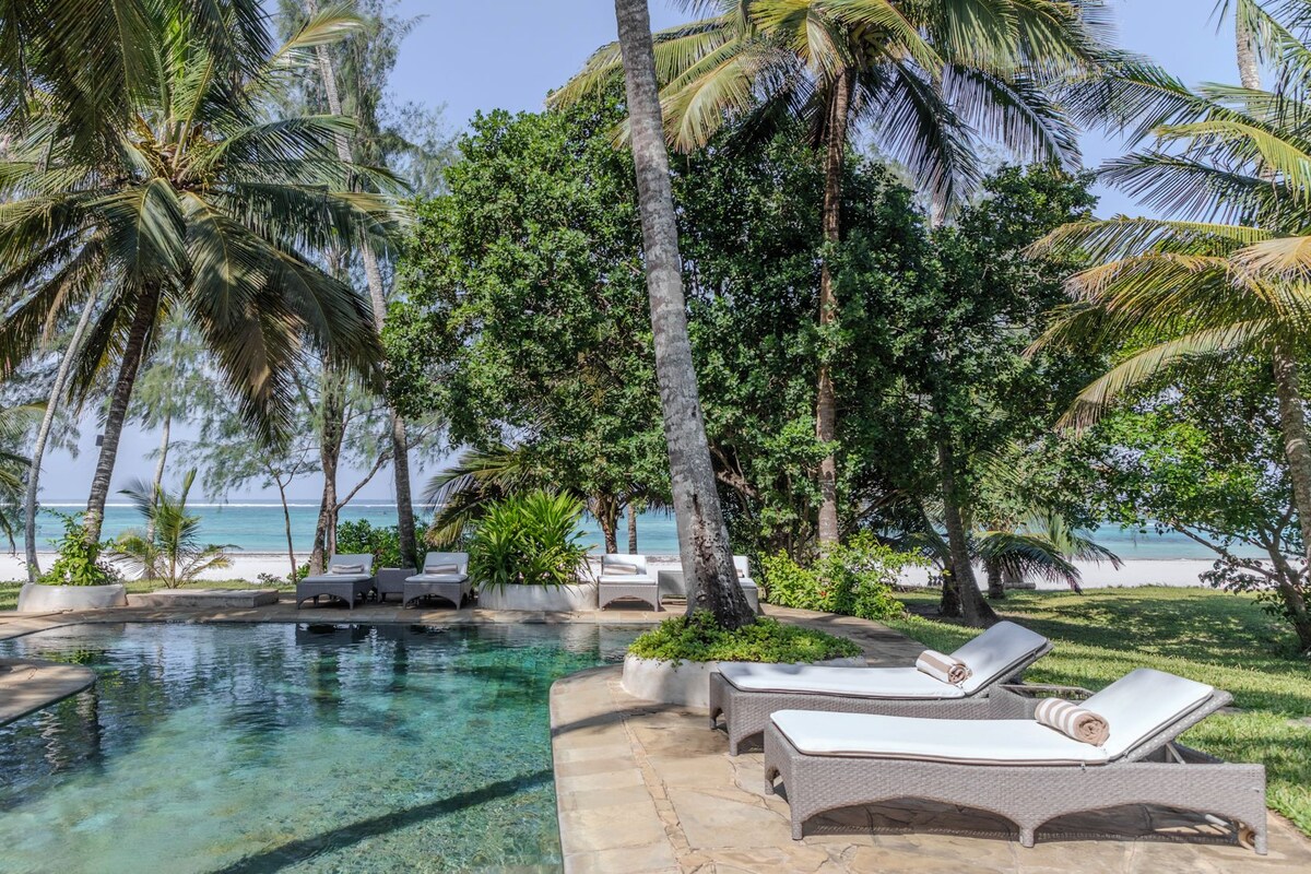 A pool area with clear water, surrounded by palm trees and lounge chairs.
