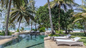 A pool area with clear water, surrounded by palm trees and lounge chairs. - Nomad Beach Resort (Diani Beach)
