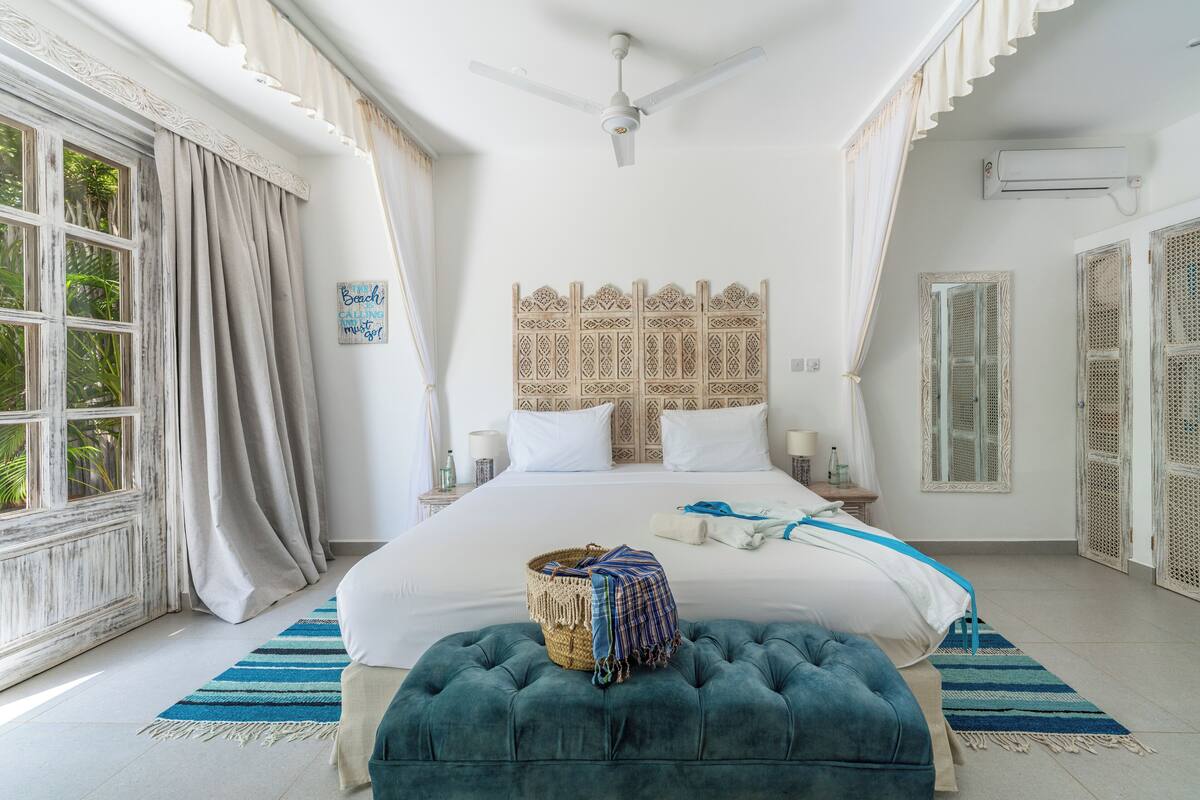 A bedroom with a large bed, a ceiling fan, a window with curtains, and a decorative headboard.