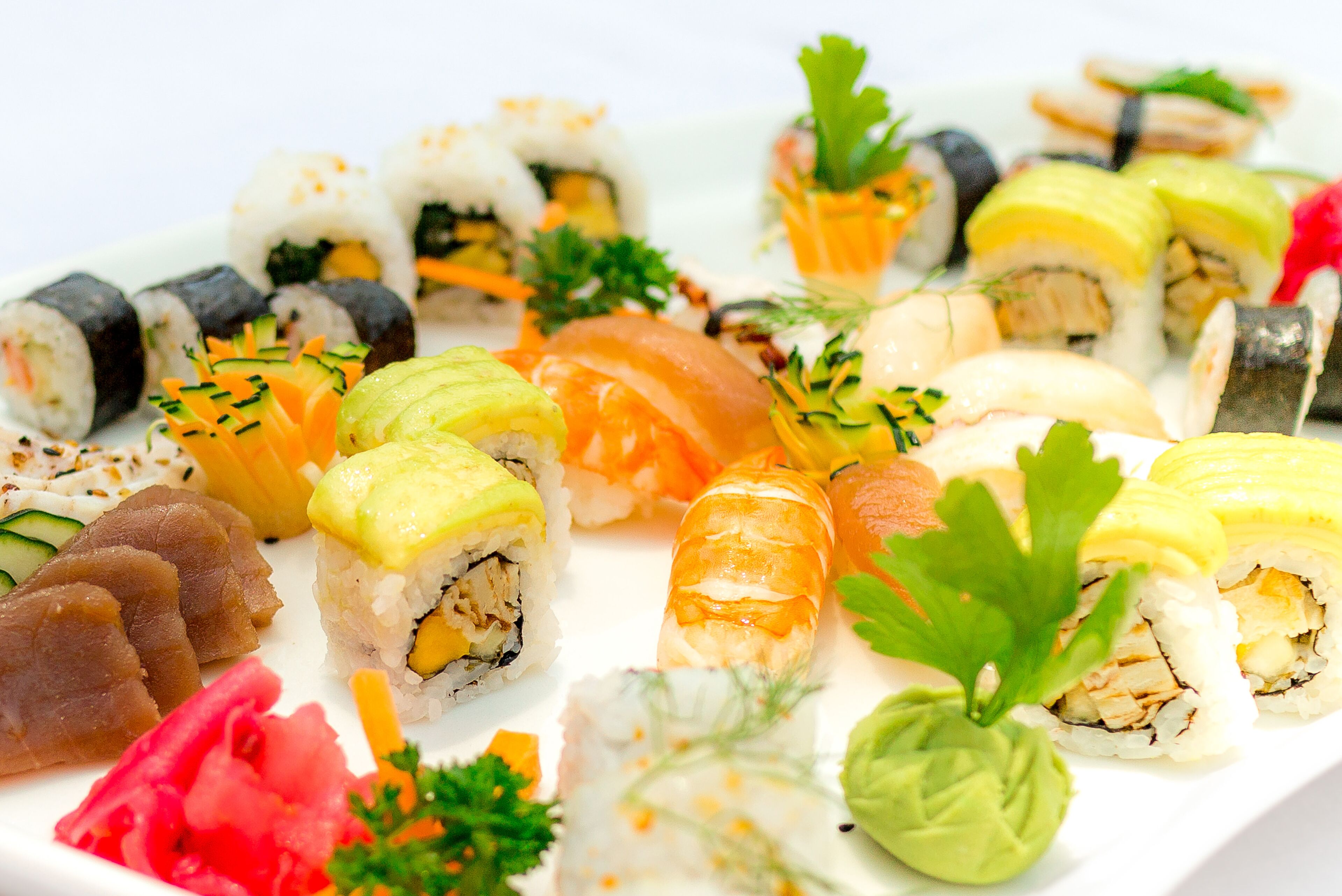 A variety of sushi rolls and sashimi on a white plate, garnished with parsley and other vegetables.