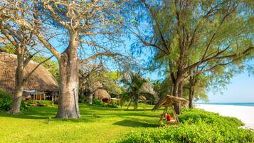 A tropical resort with thatched-roof huts, lush greenery, and a beach view.