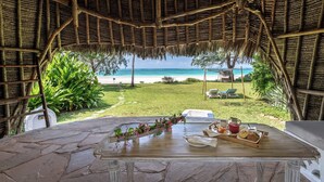 Zona de comedor al aire libre con techo de paja y vistas a la playa.