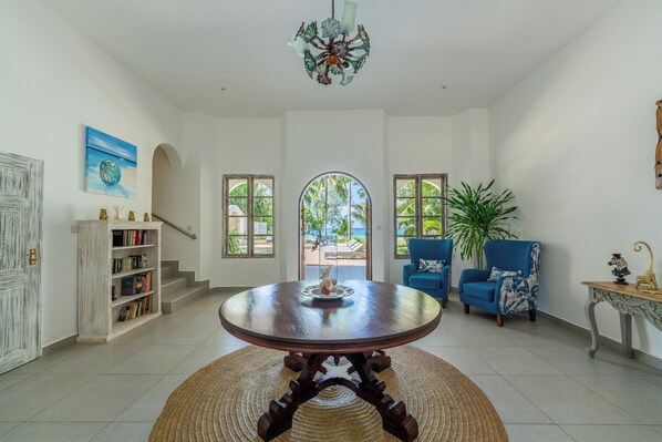 A spacious living area with a round wooden table, a bookshelf, a blue armchair, and a large plant.