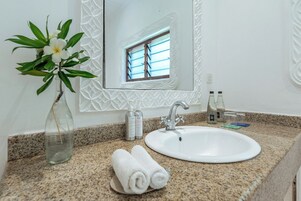 Un baño con encimera de granito, un lavamanos blanco, un espejo con marco decorativo, un florero con una flor y artículos de tocador.