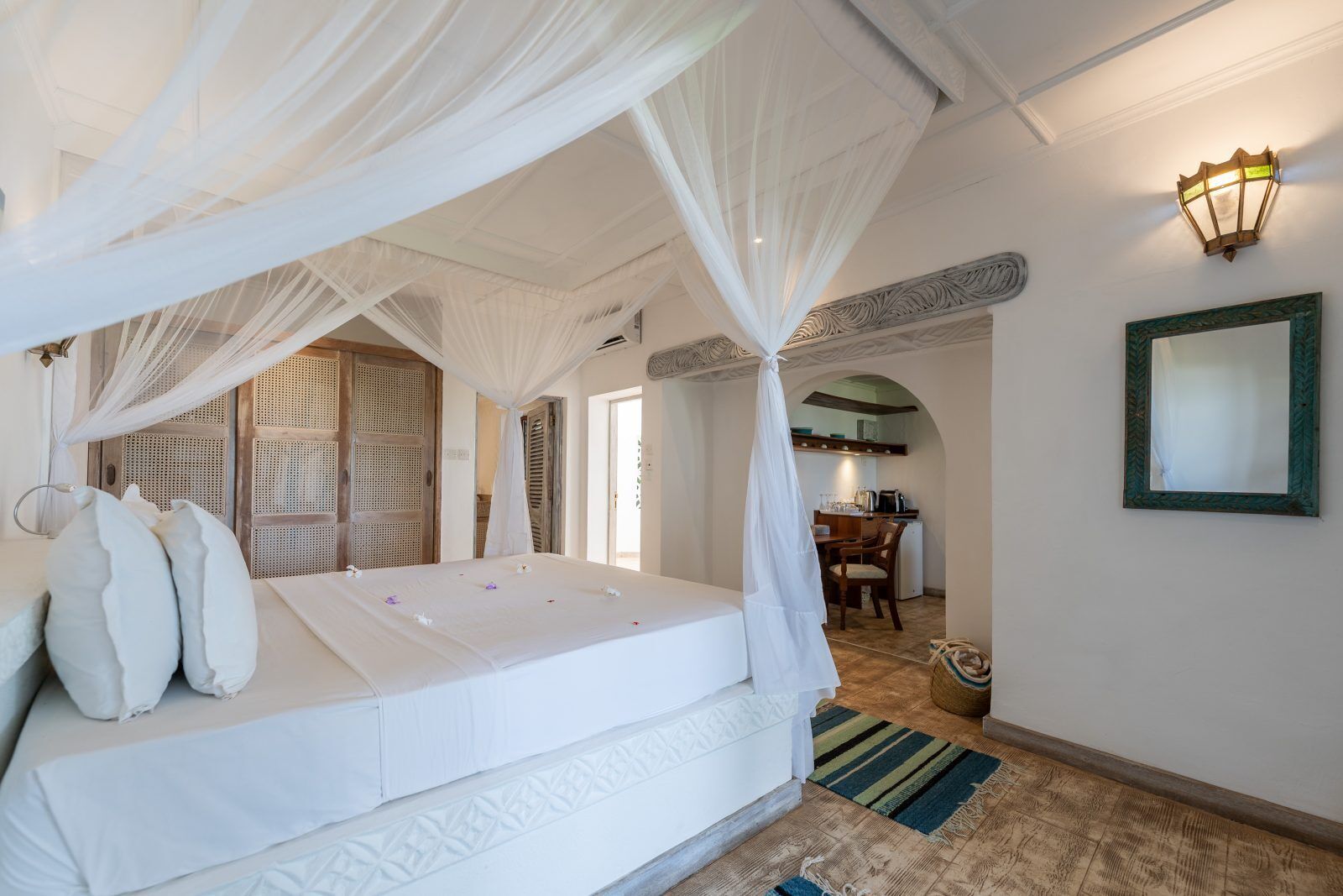 A bedroom with a canopy bed, a small kitchen area, and a mirror on the wall.
