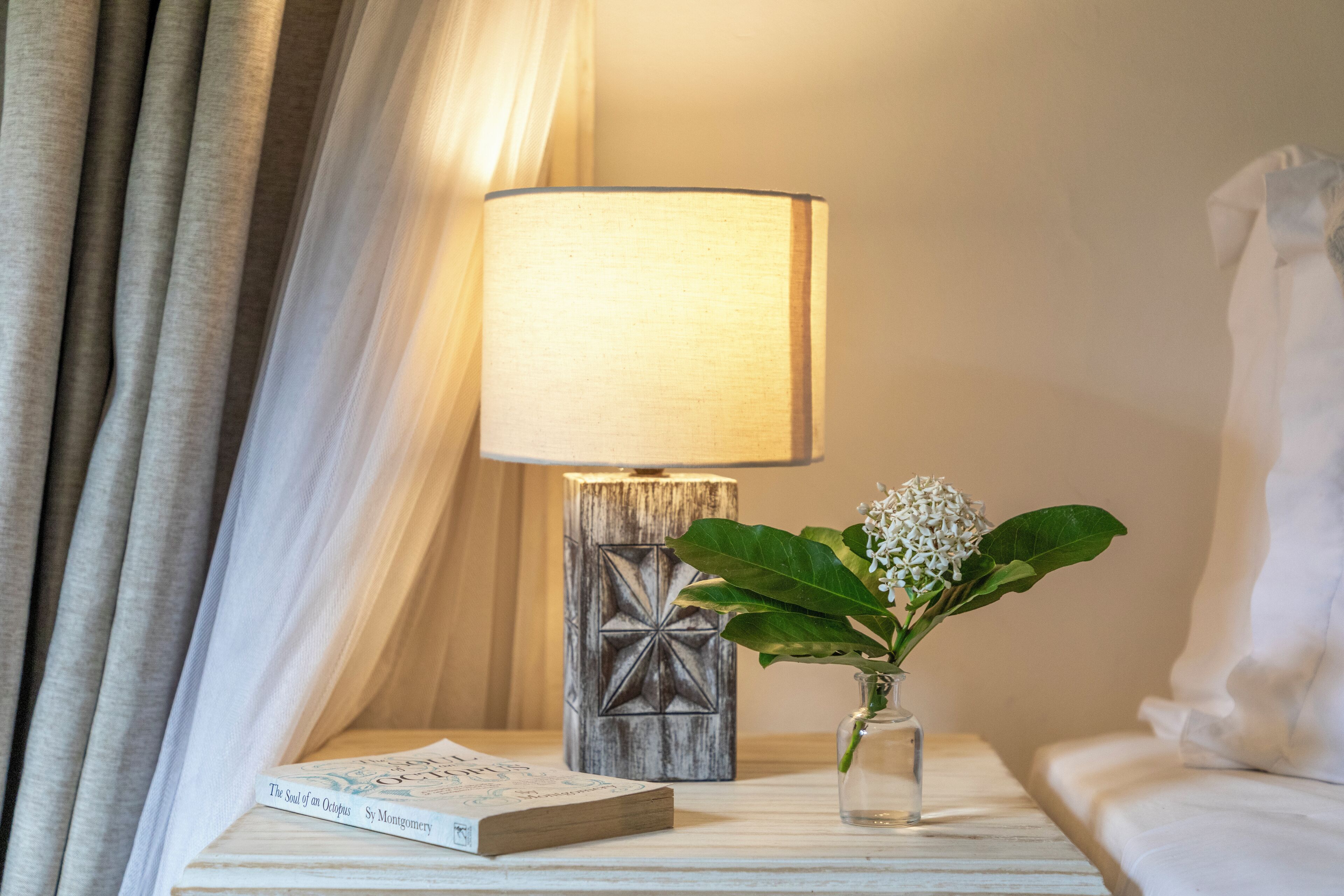 Uma mesa de cabeceira com abajur, um livro e um vaso de flores.