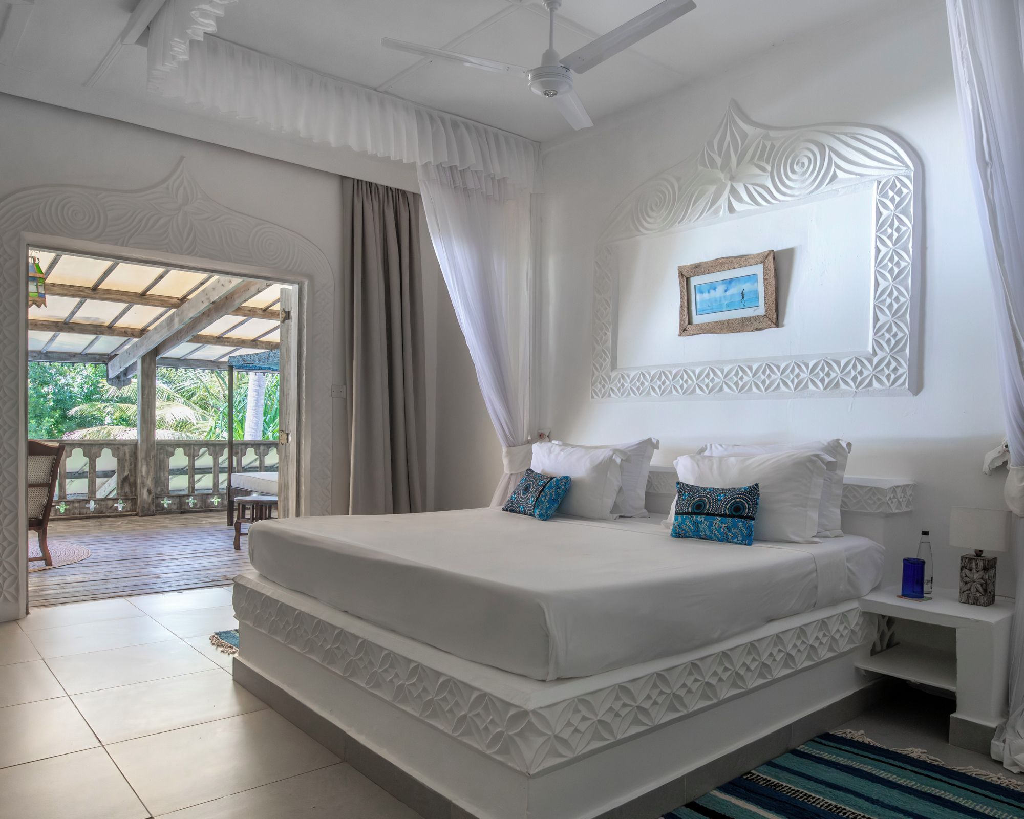 A bedroom with a large bed, a ceiling fan, a picture on the wall, and a view through the window.