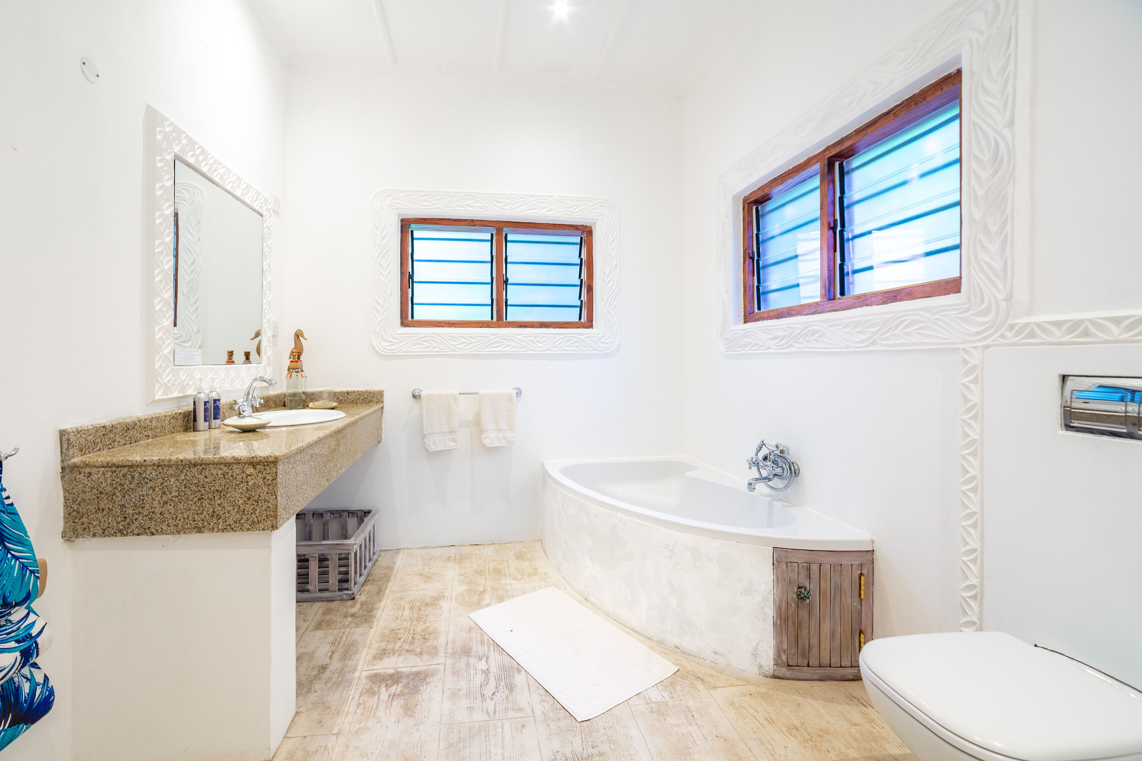 A bathroom with a granite countertop sink, a freestanding bathtub, and a toilet.