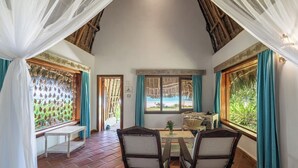 Una habitación con piso de madera, una mesa con sillas, un ventanal con cortinas y vista a la playa.