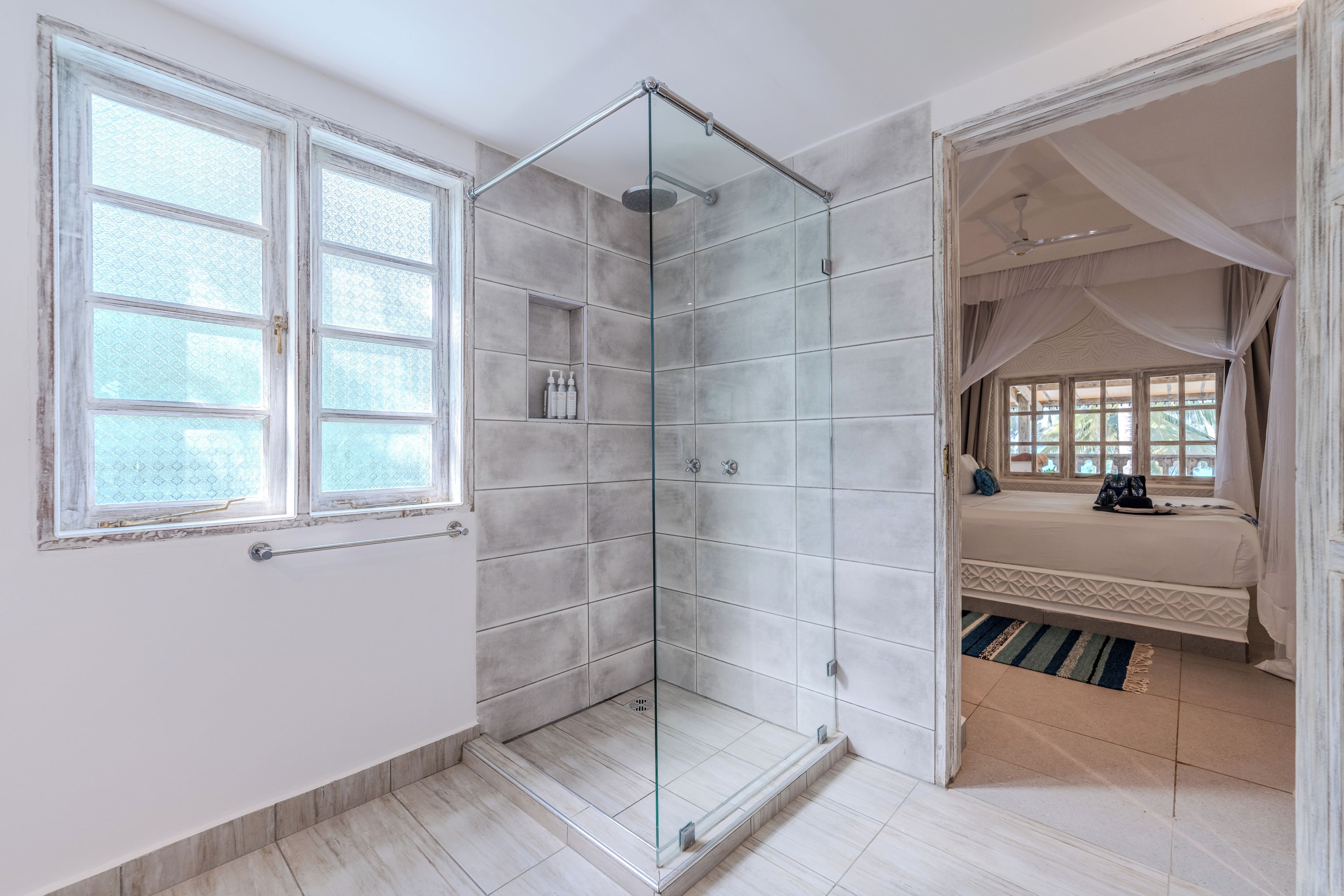 Un baño moderno con cabina de ducha de vidrio, estante empotrado con artículos de aseo y un amplio ventanal que proporciona luz natural.