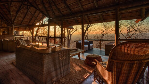 A cozy outdoor seating area with wicker furniture and a wooden deck, overlooking a scenic landscape. - Ghoha Hills Savuti (Chobe National Park)