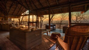 A cozy outdoor seating area with wicker furniture and a wooden deck, overlooking a scenic landscape. - Ghoha Hills Savuti (Chobe National Park)