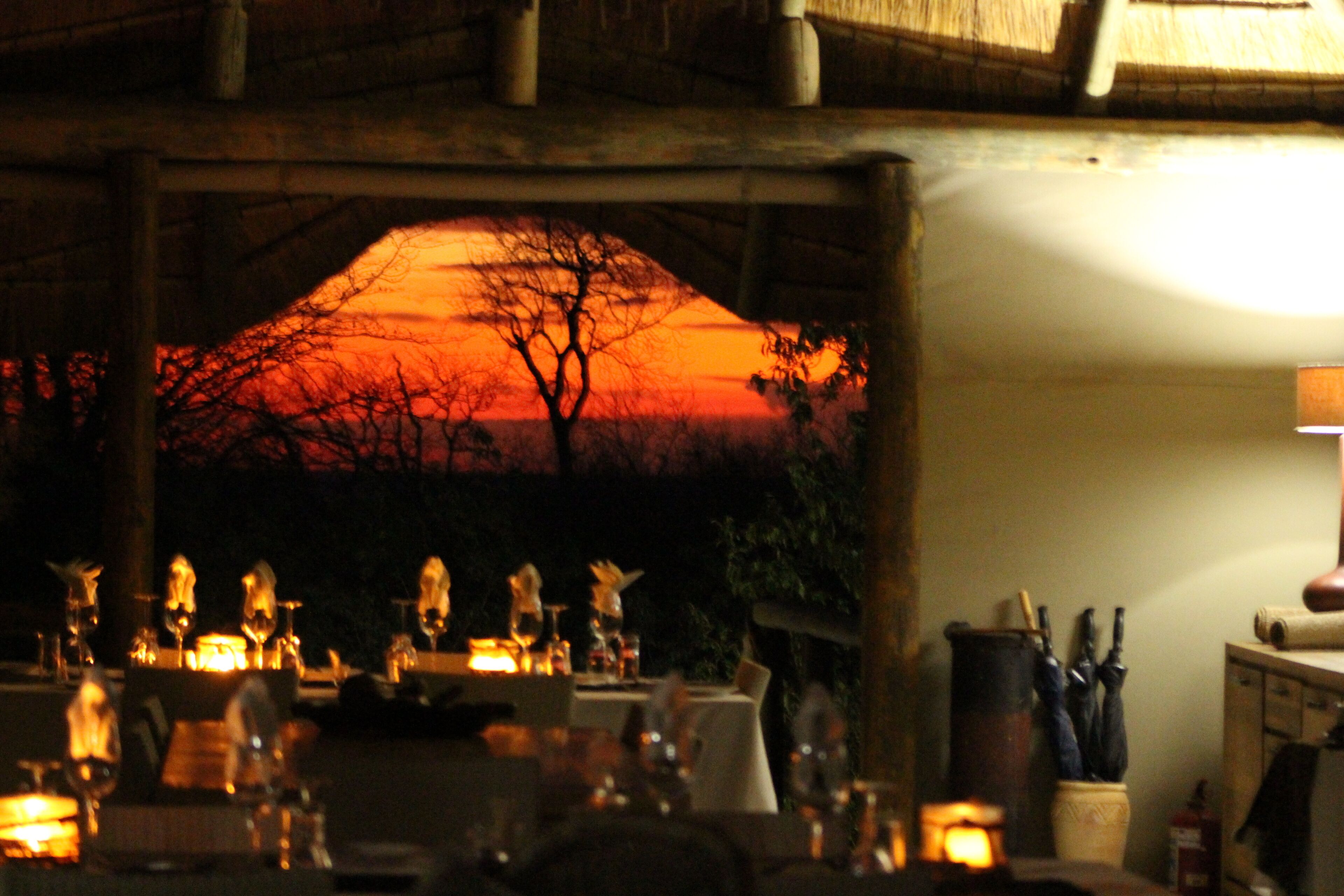 A dimly lit restaurant with a view of a sunset through an archway.