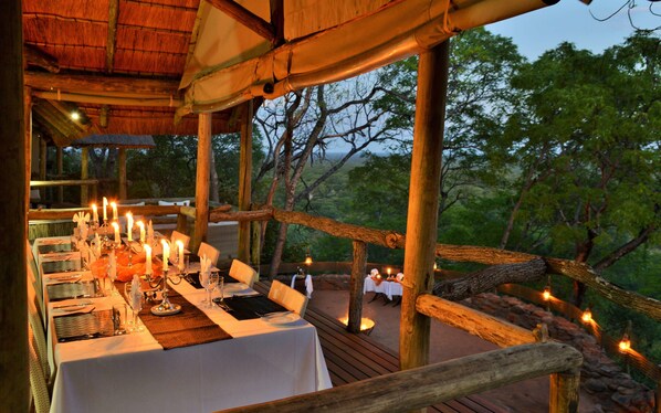 An outdoor dining area with tables set for a meal, surrounded by wooden railings and natural scenery. - Ghoha Hills Savuti (Chobe National Park)