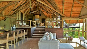 A rustic interior with a thatched roof, wicker furniture, and a staircase leading to a balcony. - Ghoha Hills Savuti (Chobe National Park)
