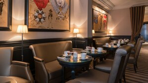 Un vestíbulo de hotel con asientos de cuero, mesas con vajilla de té y obras de arte históricas enmarcadas en las paredes.