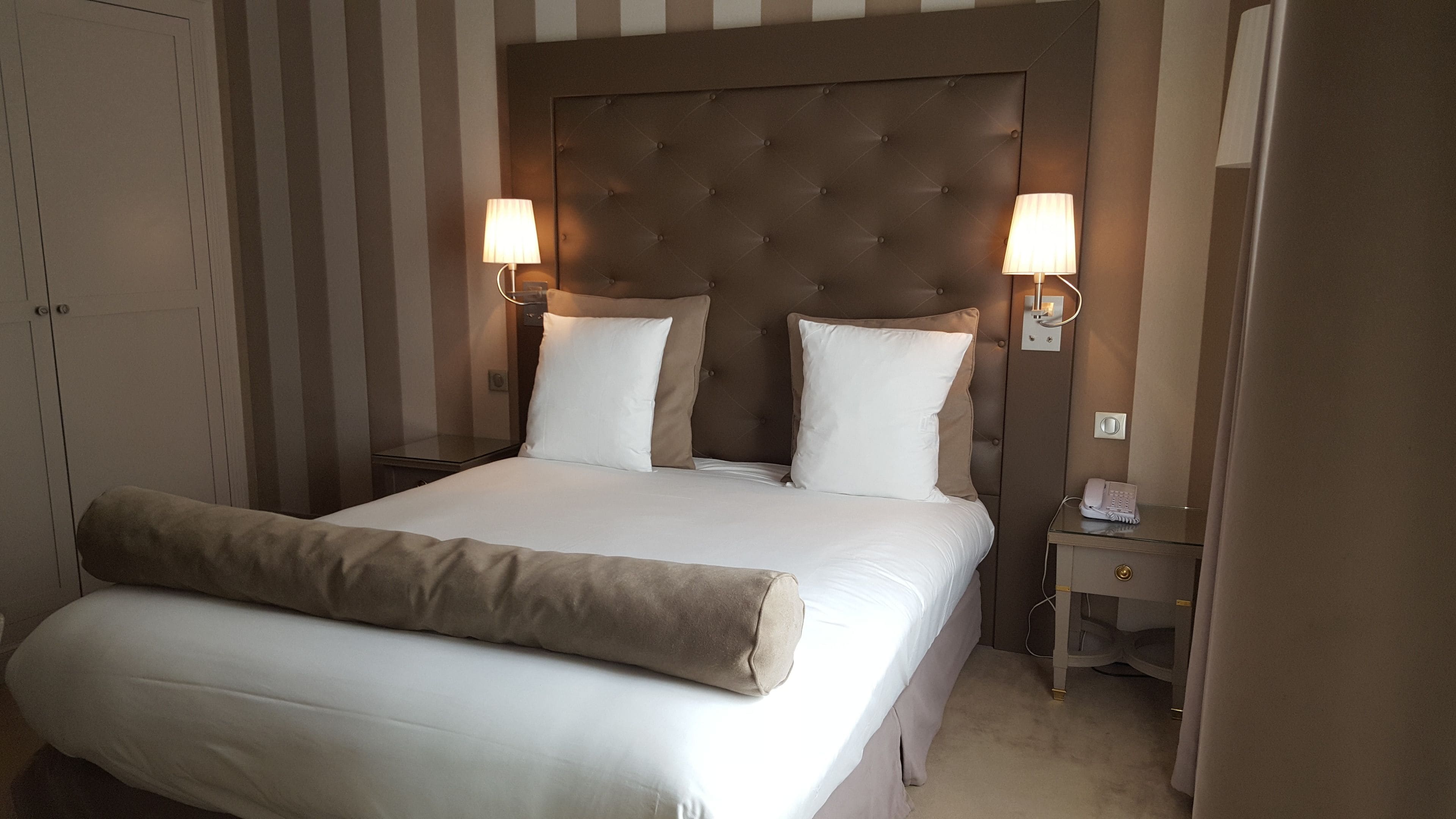 Una habitación de hotel con una cama grande, dos lámparas de noche, una mesita de noche y una puerta.