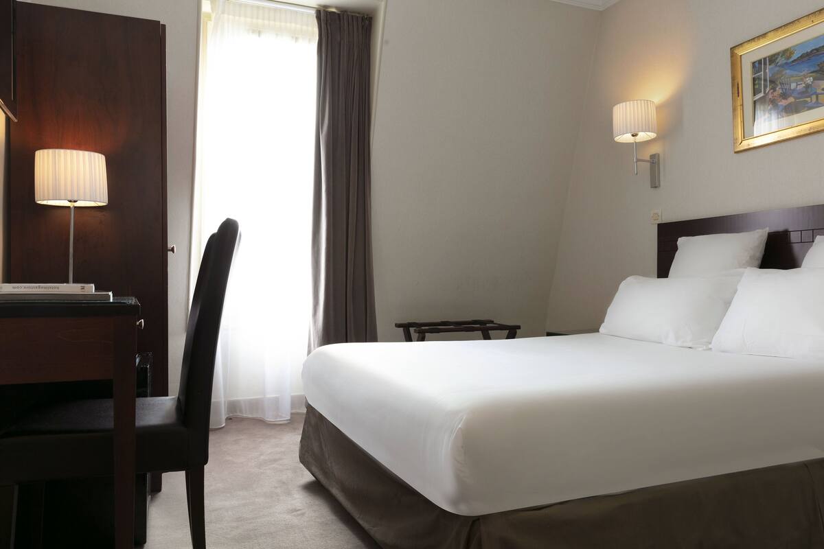 A hotel room with a bed, a desk, a chair, and a lamp.