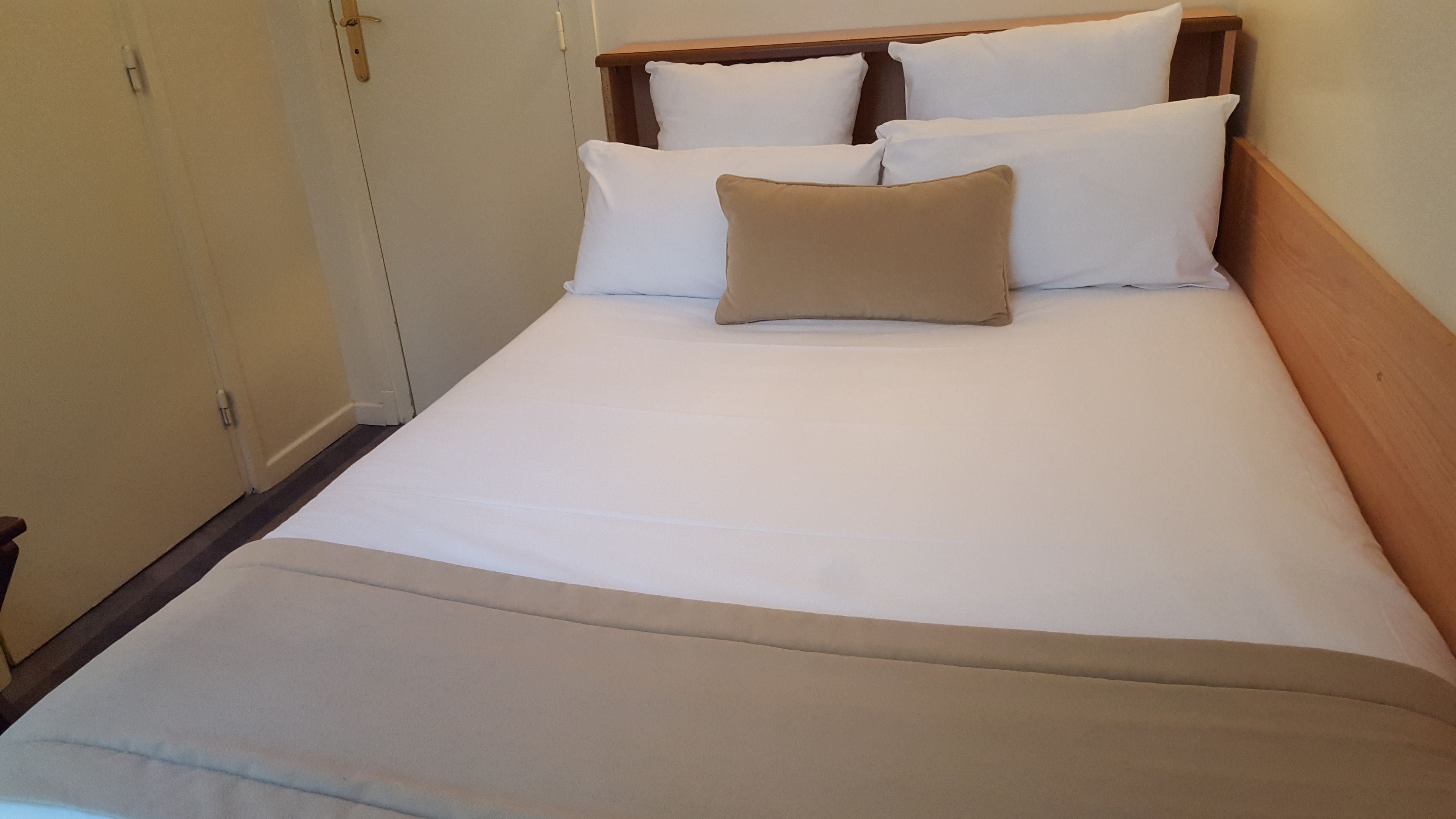 Un lit simple avec une tête de lit en bois, une literie blanche et un plaid beige.