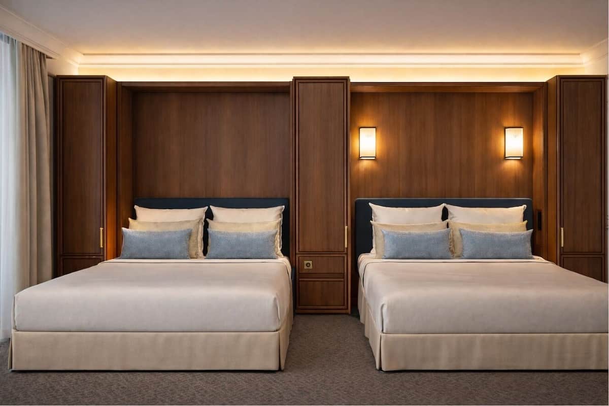 A hotel room with two beds, wooden paneling, and wall-mounted lights.