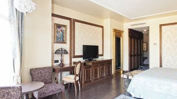 Habitación de hotel con cama, escritorio con televisor, silla, una mesita redonda y un tapete decorativo.